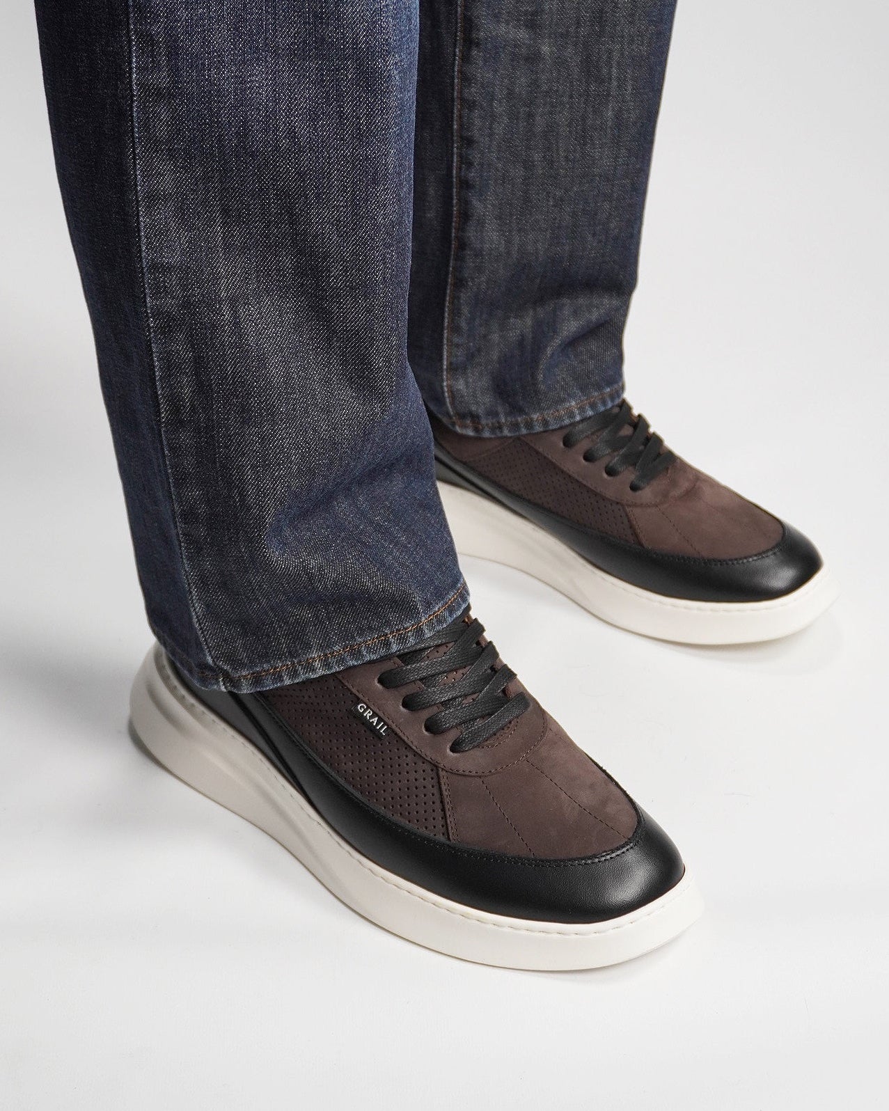 Brown sneakers with black soles worn with blue jeans on a light gray background