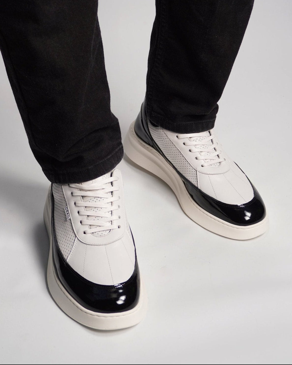 White sneakers with black soles worn with black pants on a light gray background